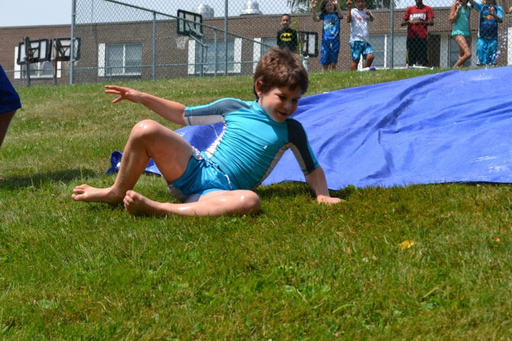 A boy from a Christian school is playing with a blue tarp in the grass.