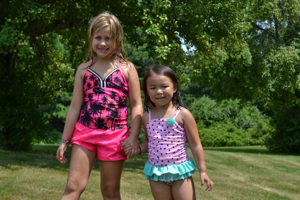 Two little girls in swimsuits standing in a grassy area at a Christian school.