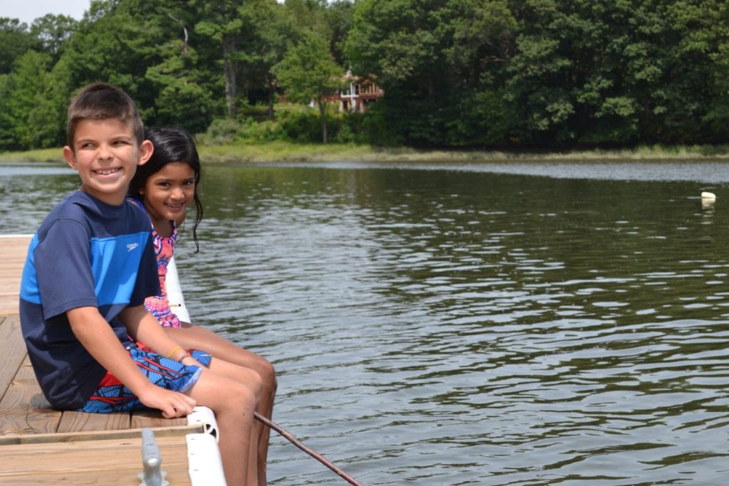 Two children from a Christian school sitting on a dock with fishing poles.
