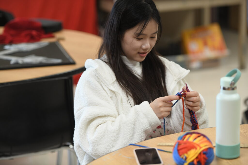 An upper school student doing a knitting activity