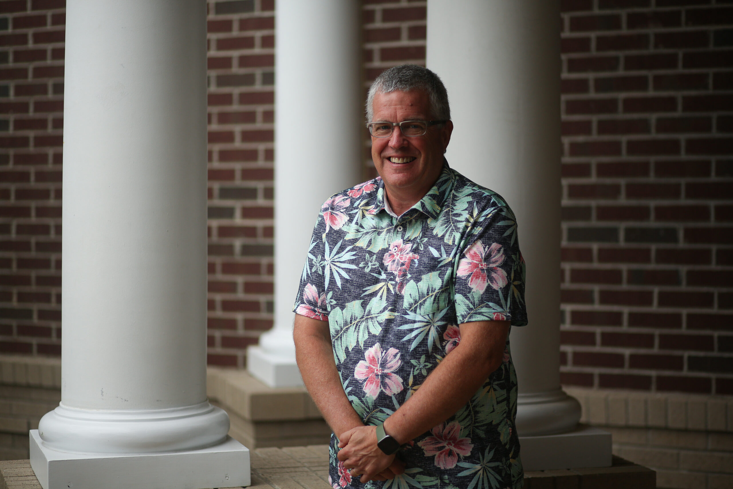 A man wearing a Hawaiian shirt attends his child's graduation ceremony at a Christian school.