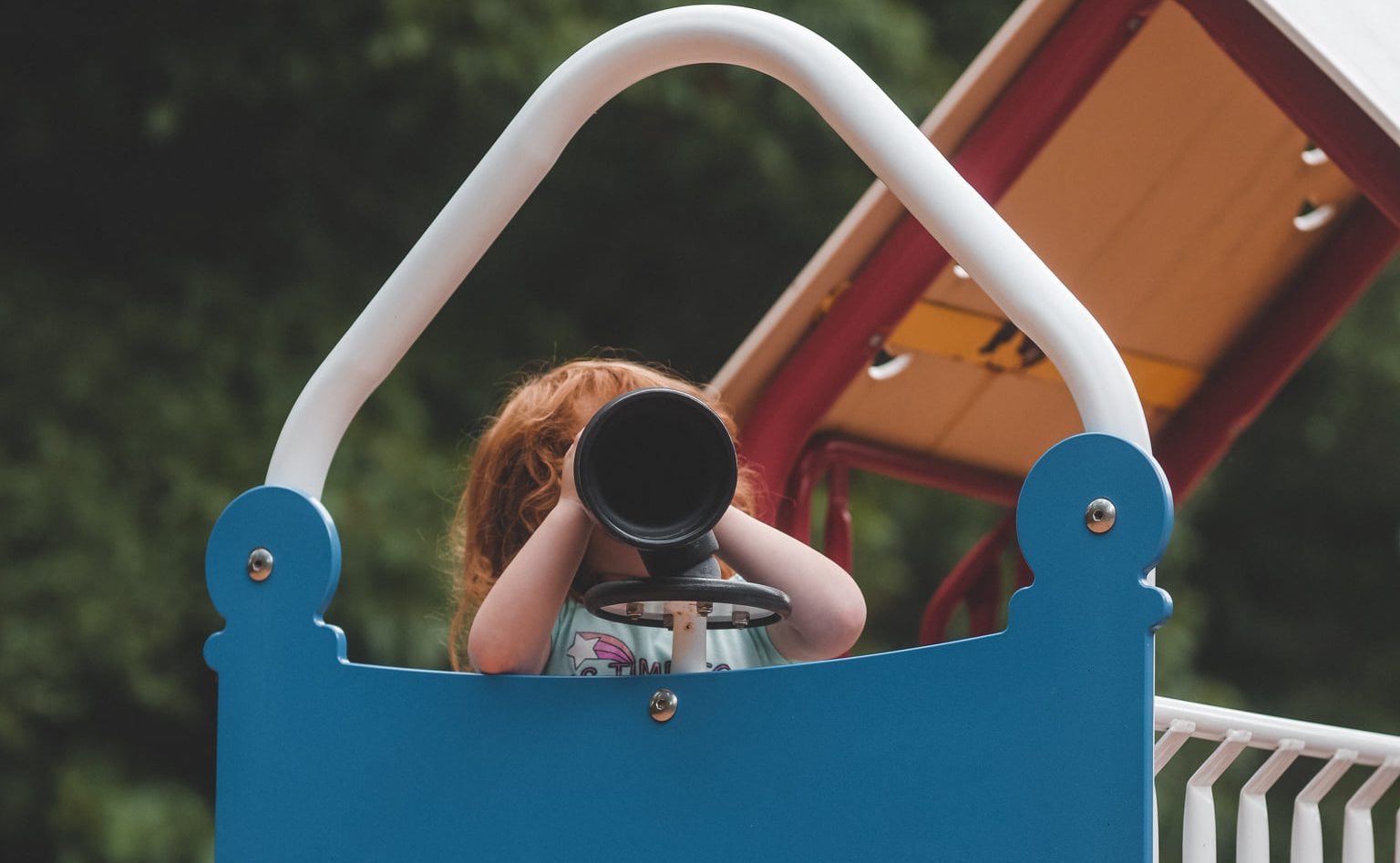 A preschool student in the playground looking over a toy telescope