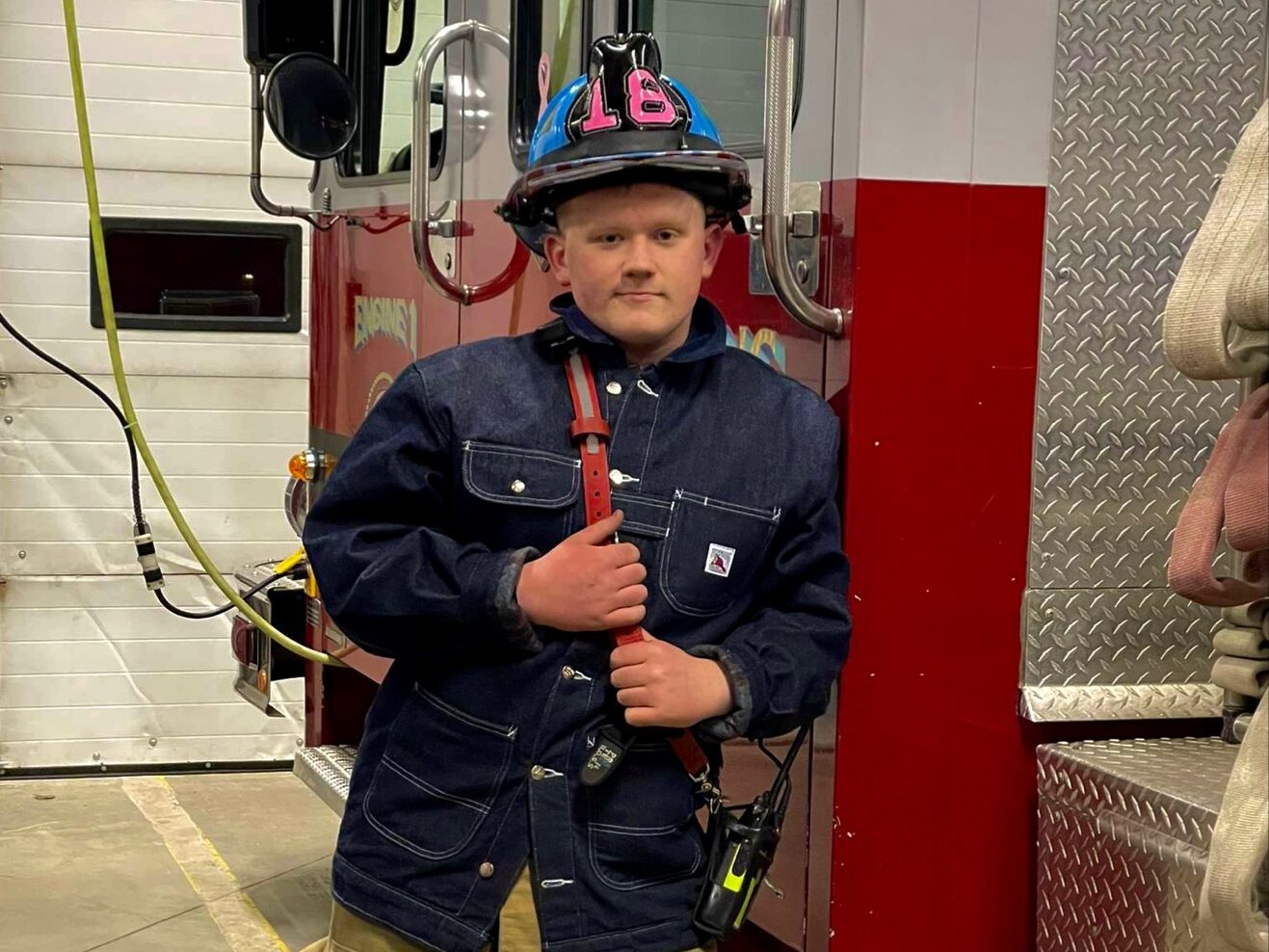 A young man in a firefighter uniform standing next to a fire truck.