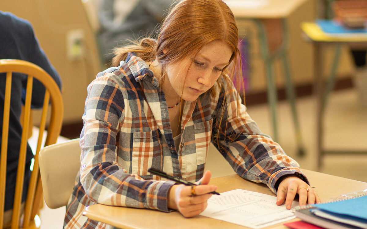 A girl sitting at a desk and writing on a piece of paper.