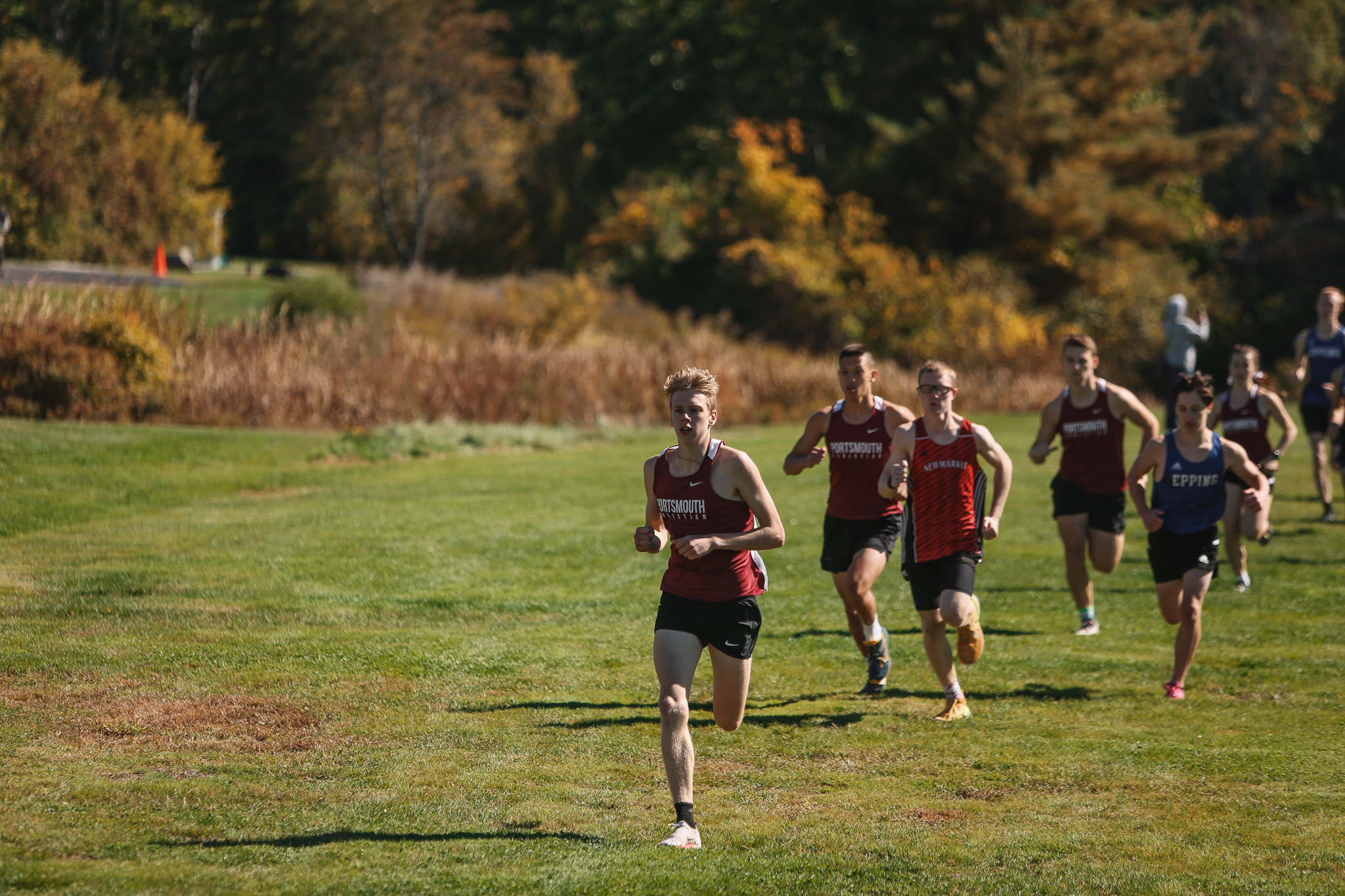 A group of cross country runners running on a grassy field.