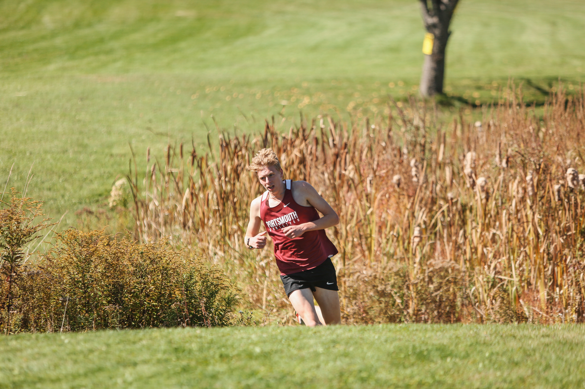 A man in a maroon shirt is running in a grassy field.
