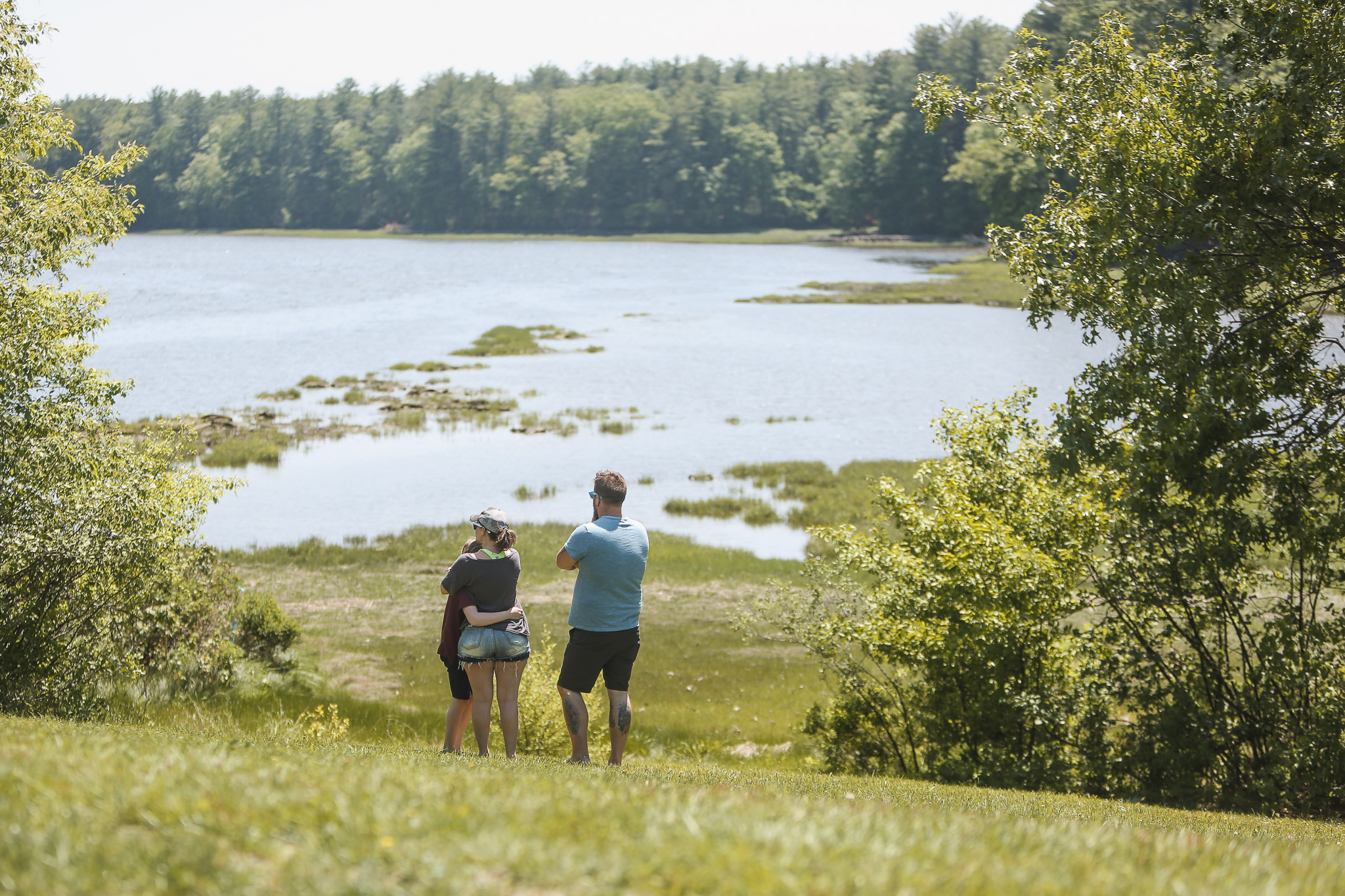 Two people walking on a grassy hill near a lake.