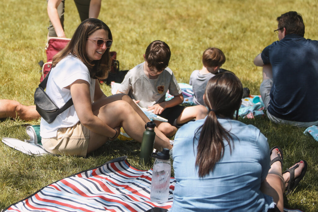 A group of people sitting on a blanket in the grass.