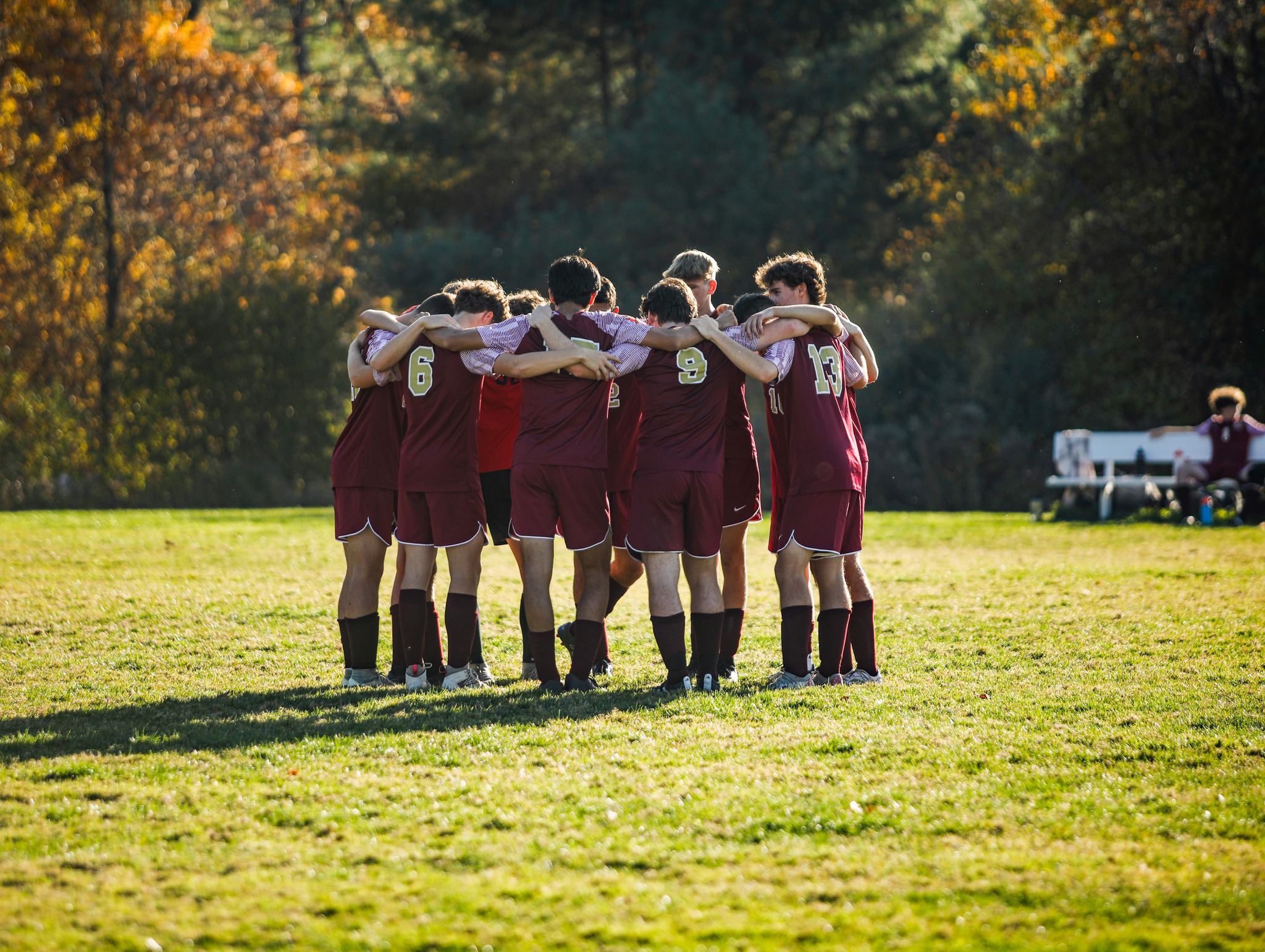 A man in a maroon jacket and cap high-fives students standing in a line outside a brick building.