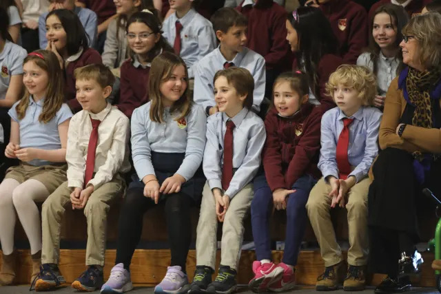 A man with a guitar and a woman with a microphone stand on stage in front of a screen displaying "Martin Luther King Jr." as an audience watches.