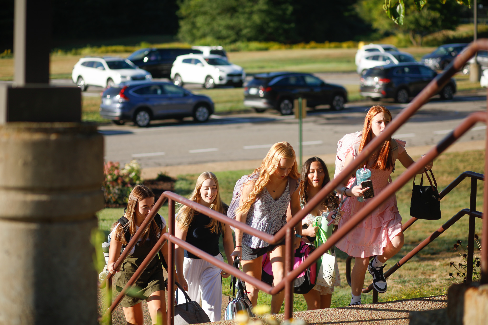 A man in a maroon jacket and cap high-fives students standing in a line outside a brick building.