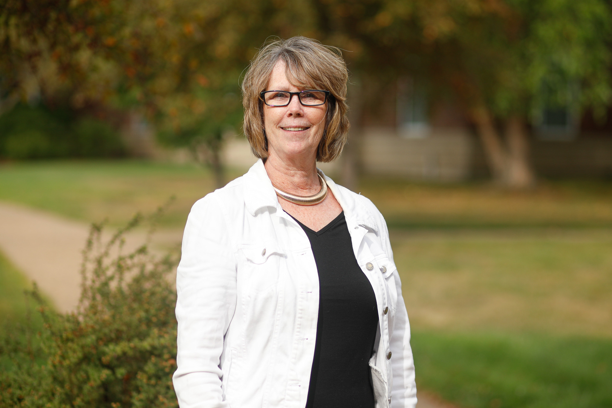 A smiling woman in a dress standing in front of trees, representing a Christian school.