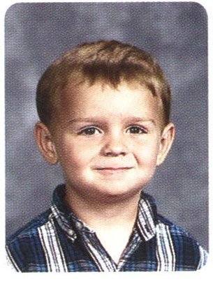 A black-and-white portrait of a young boy with short hair, smiling and wearing a striped shirt, with an oval border around the image.