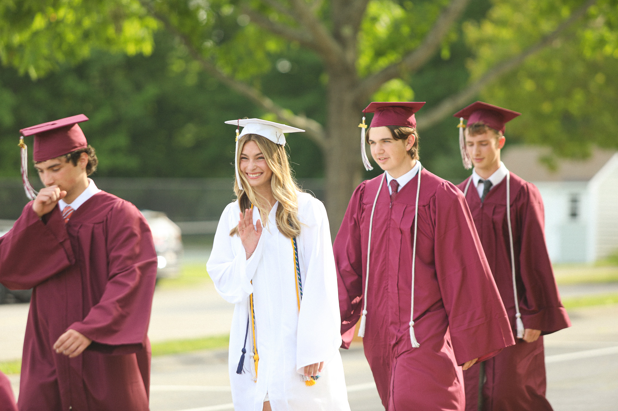 A group of people in academic robes descends stairs outside a building, with greenery and flowers surrounding the area.