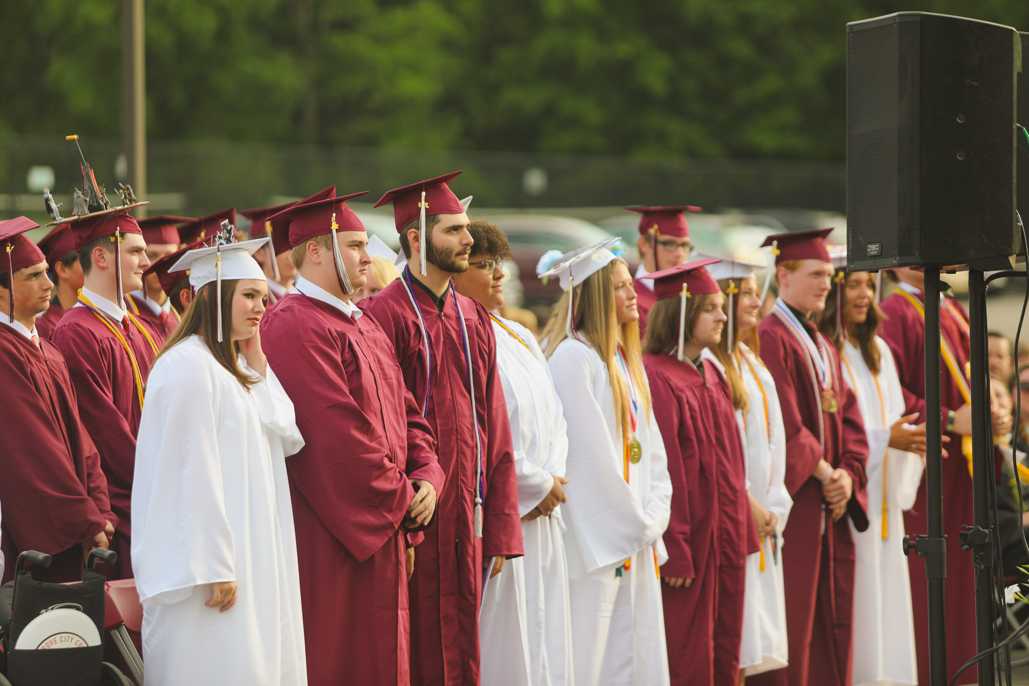 A graduate in a maroon cap and gown holds a diploma and poses with three people, likely family members, in front of a projected school emblem.